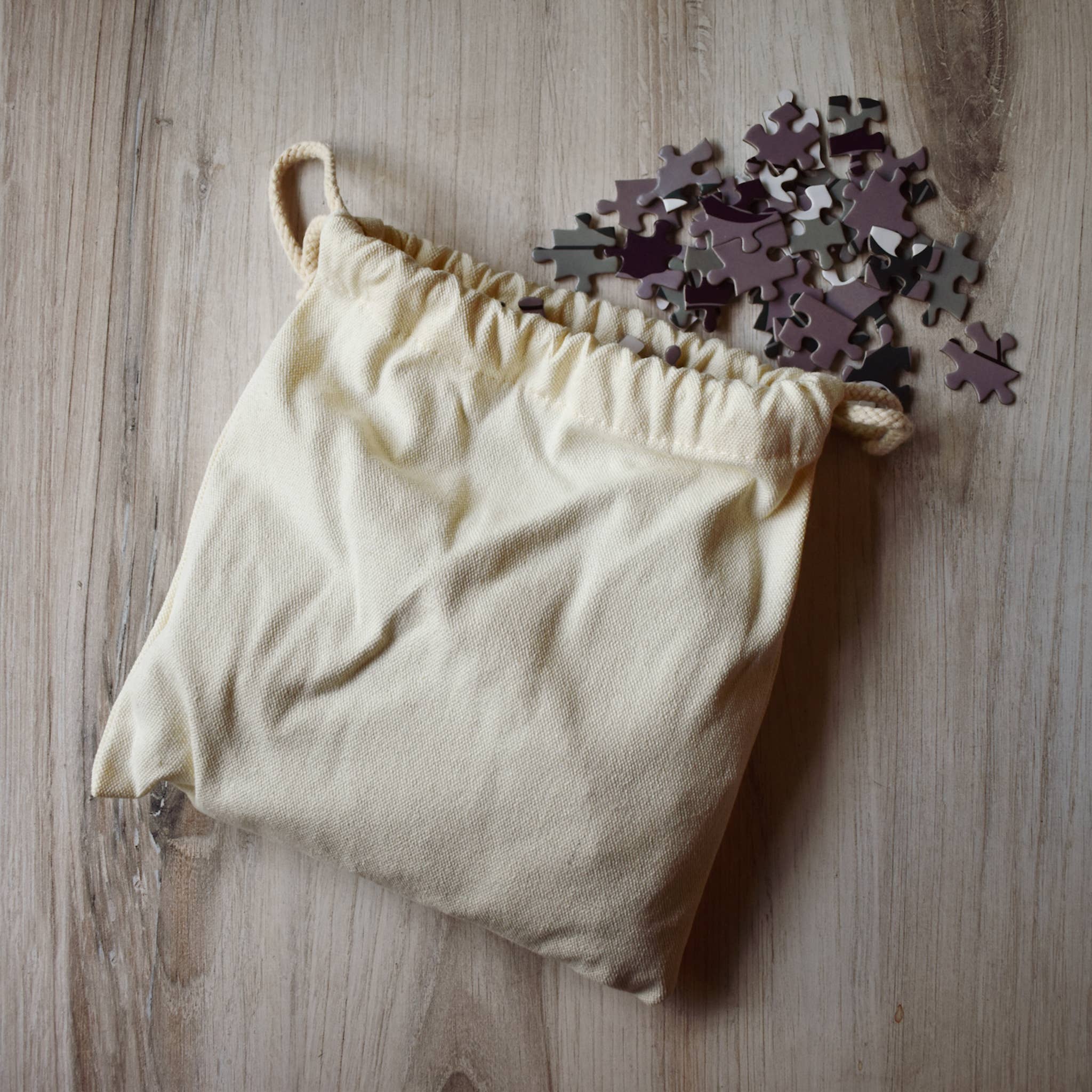 Beige drawstring bag with puzzle pieces on a wooden surface