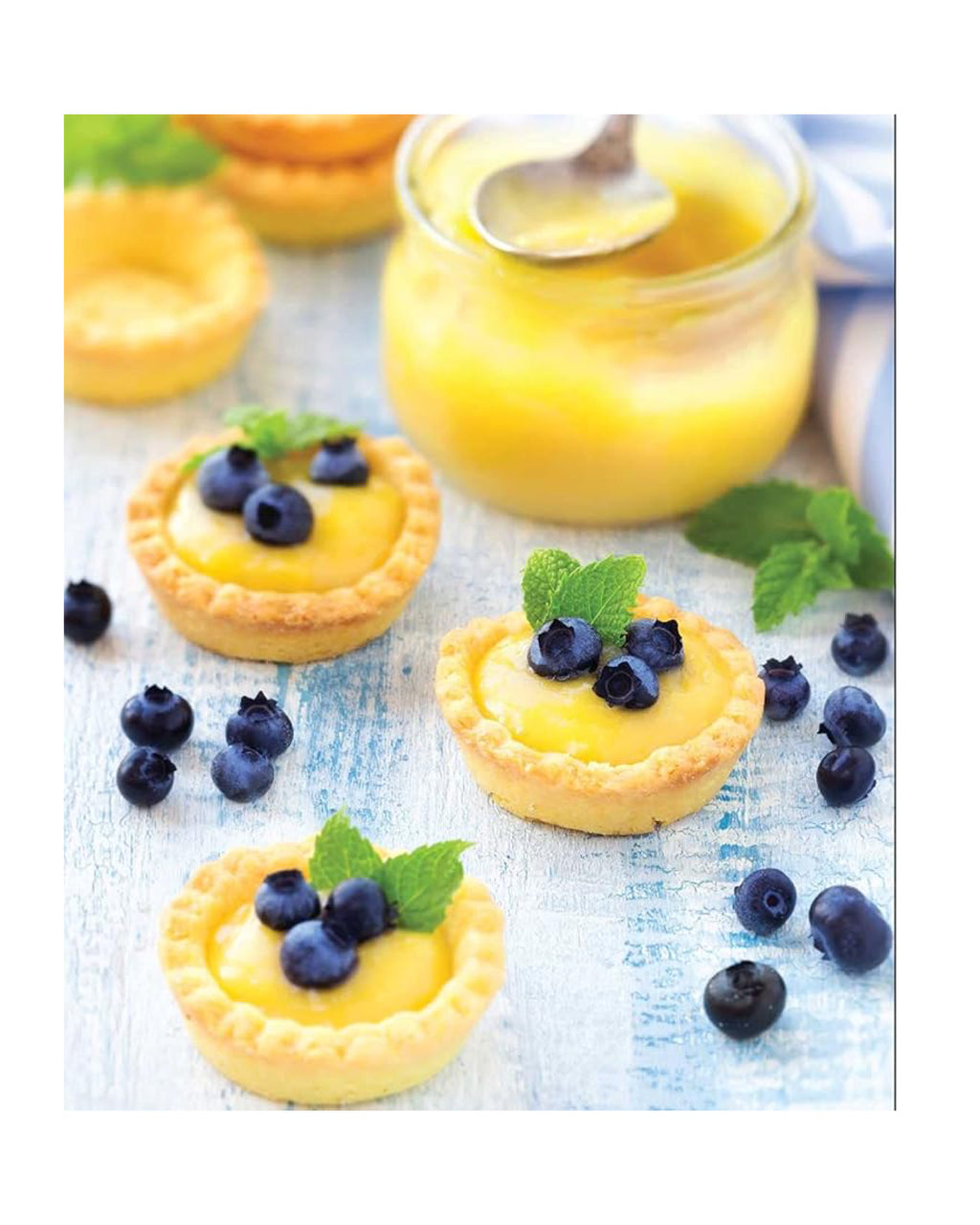 Small lemon tarts with blueberries and mint leaves on a light surface.