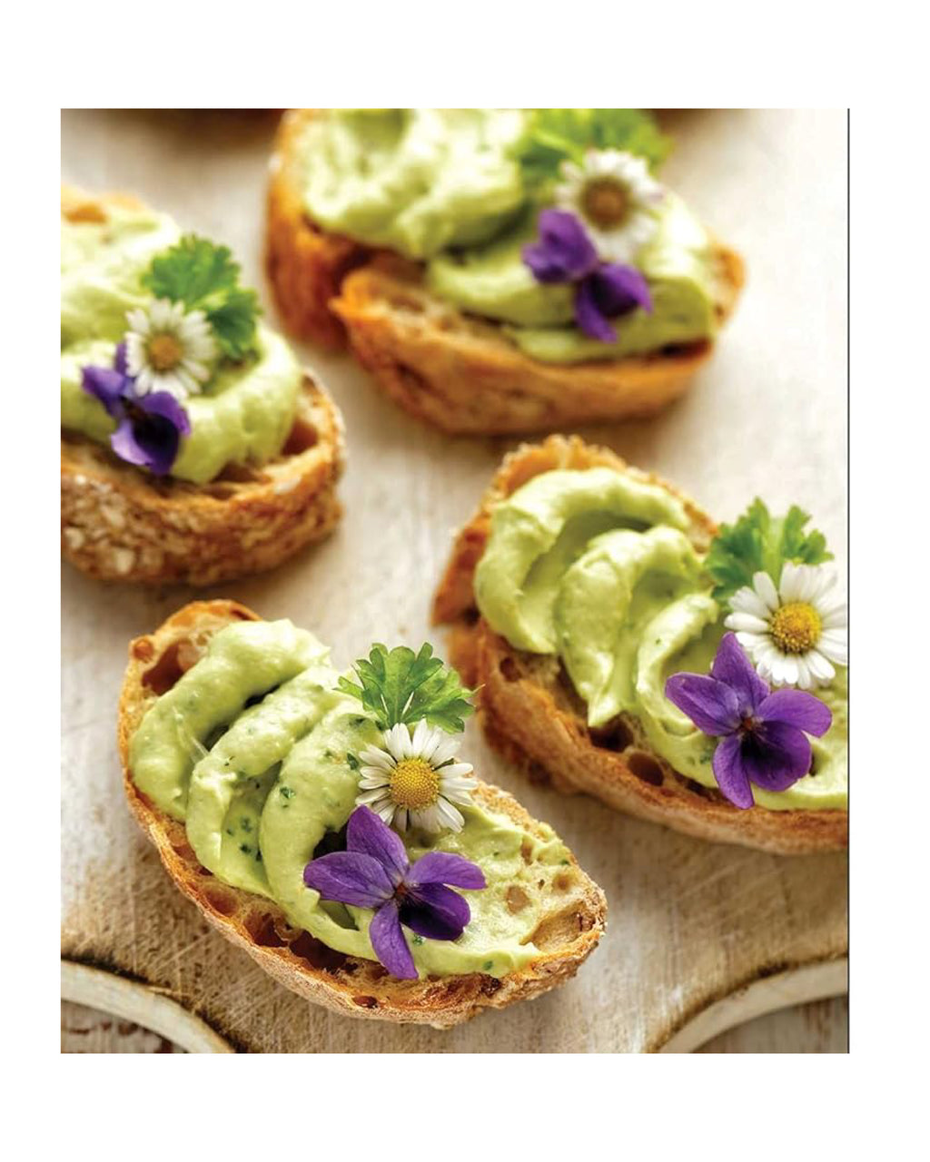 Small toasts with avocado spread and garnished with flowers on a textured surface.