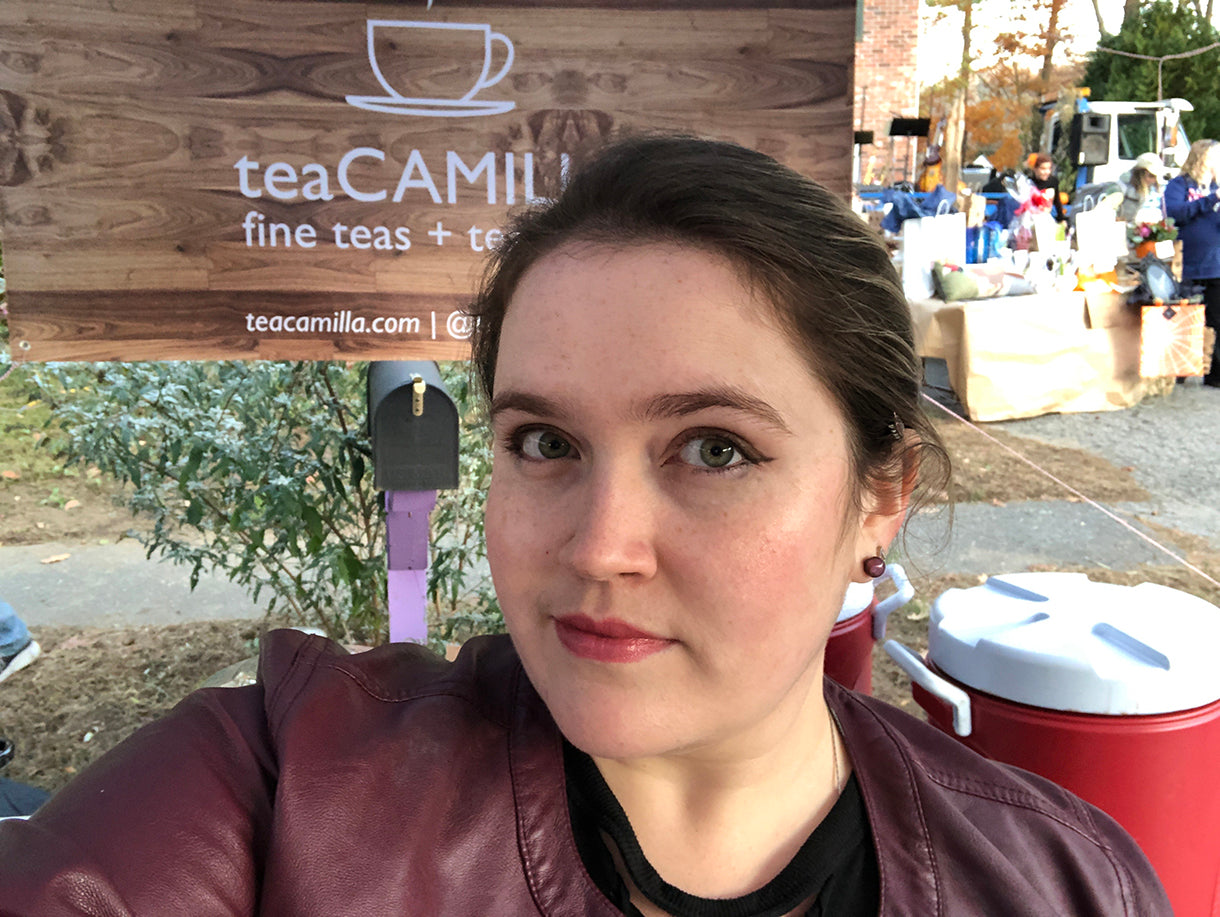 Woman in front of a wooden sign with 'teaCAMILIA' branding