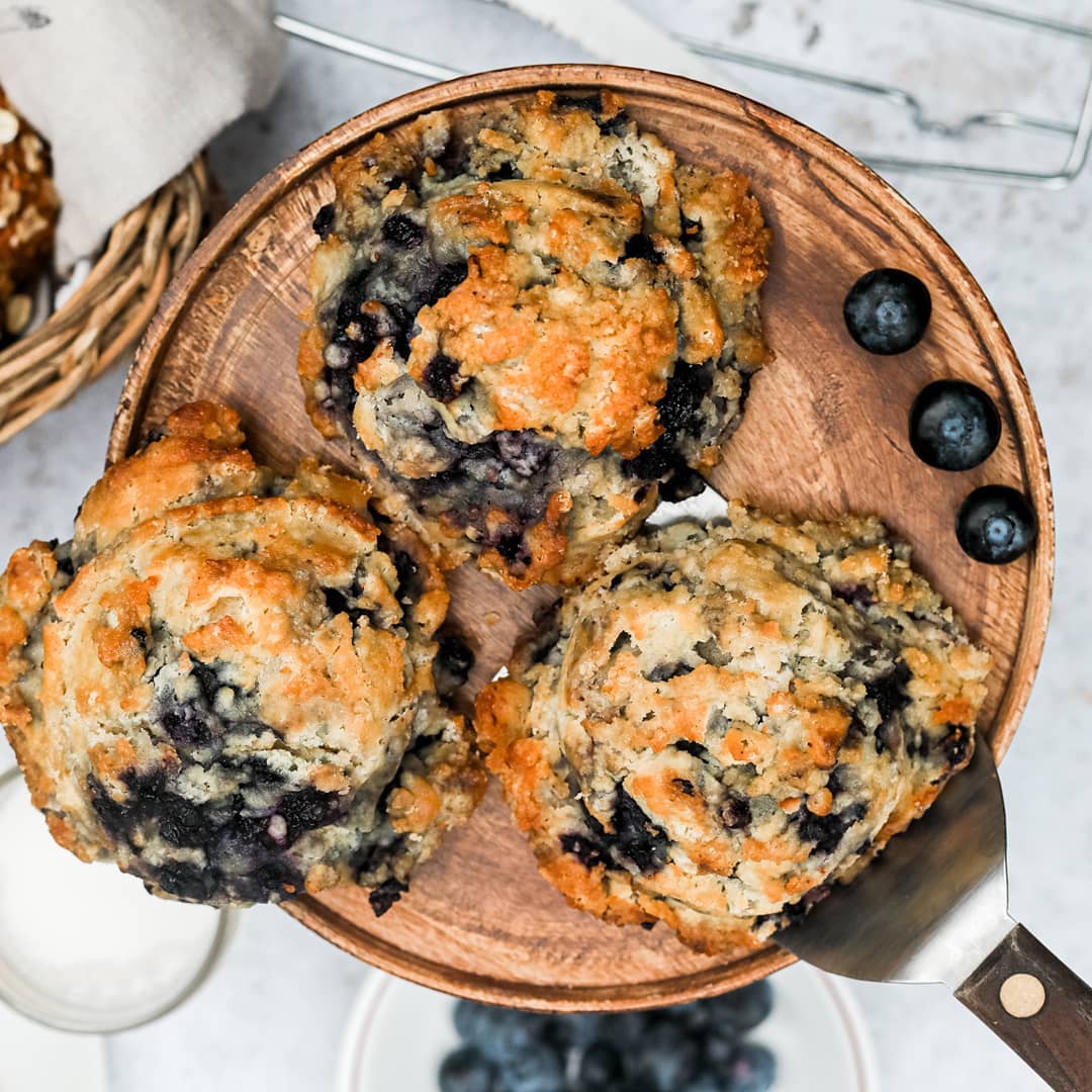 Blueberry muffins on a wooden plate with blueberries around